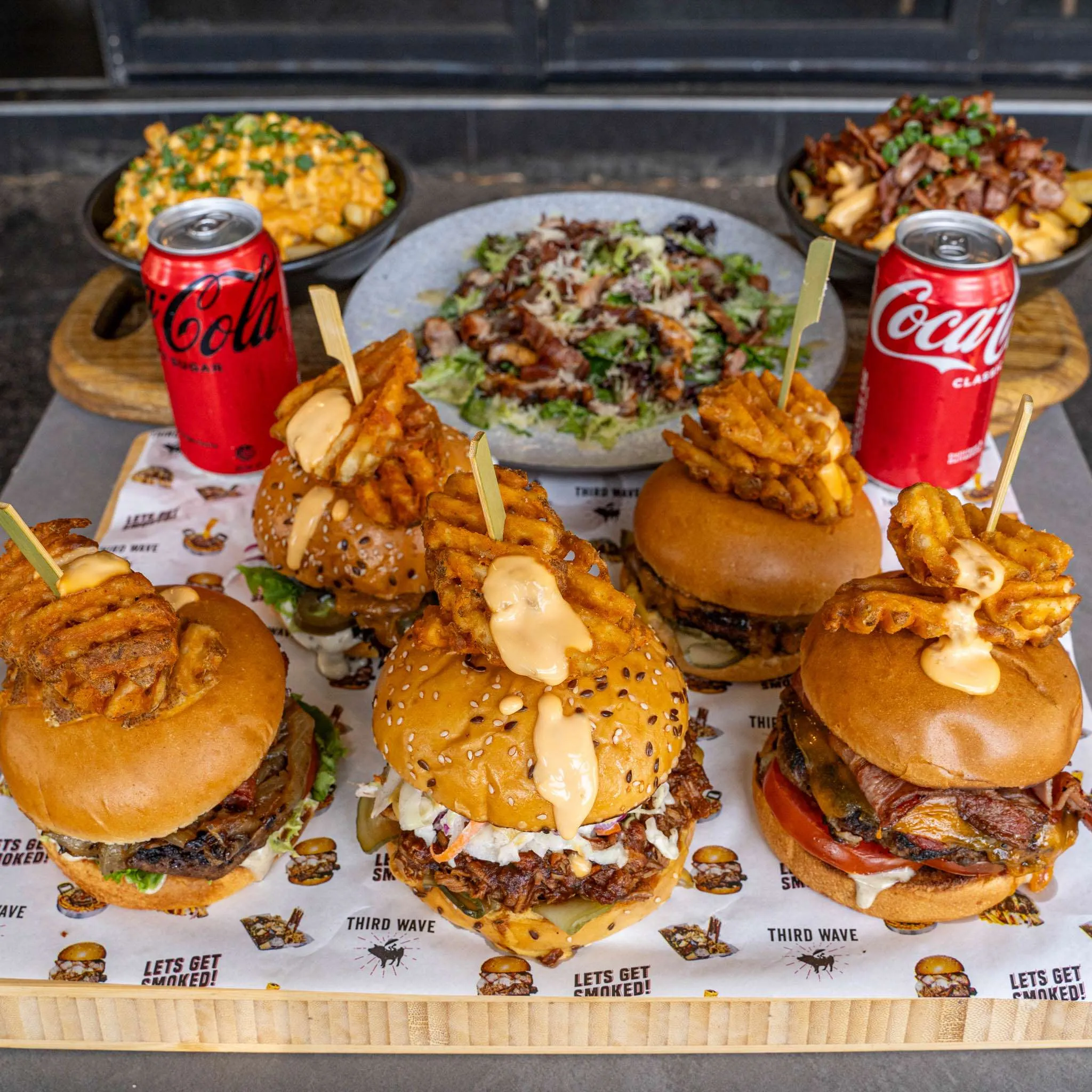 Sliders, Mac & Cheese, salad and cola arranged on a board